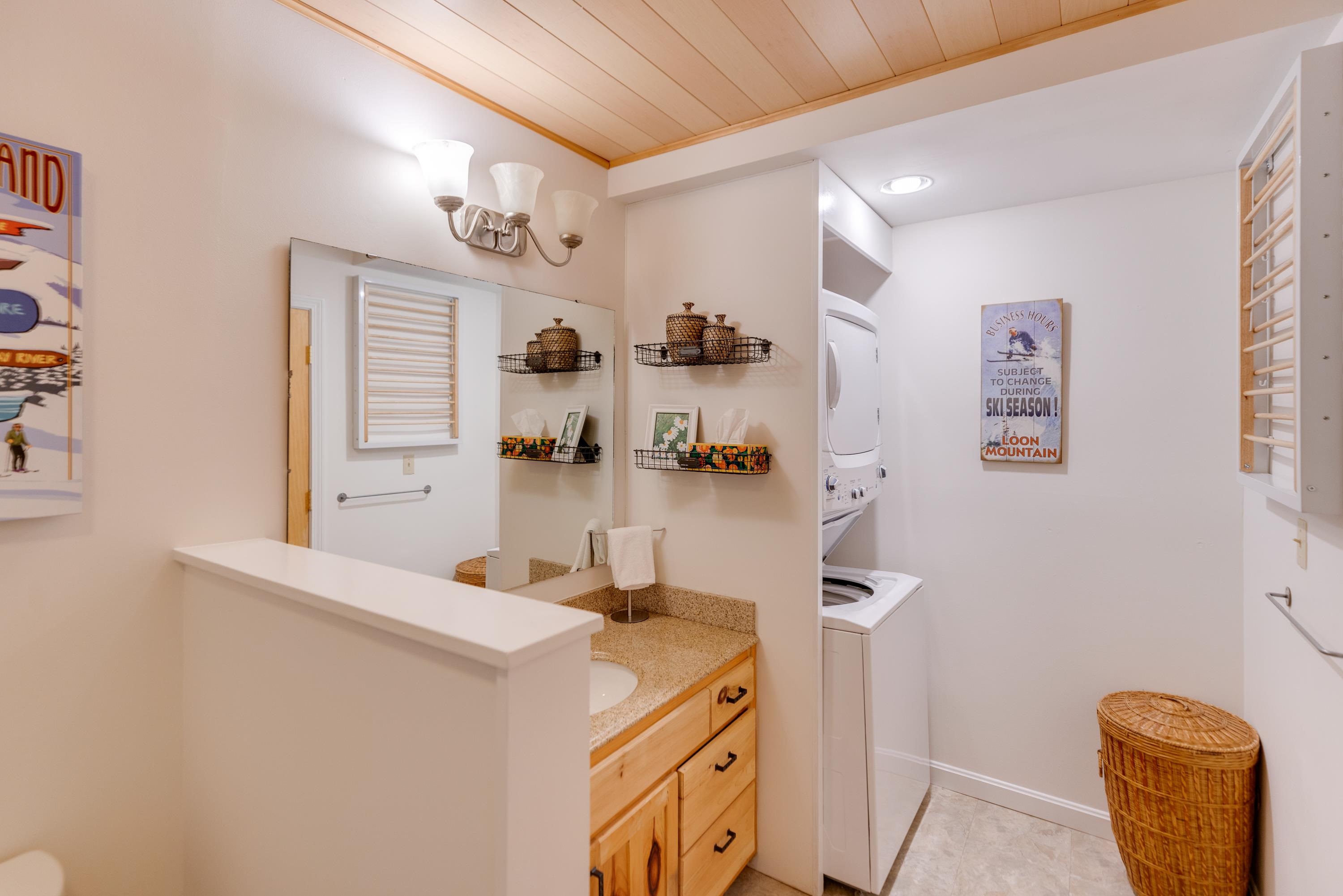 Laundry room with washer and dryer beside a wood-cabinet vanity under a sloped wood ceiling.