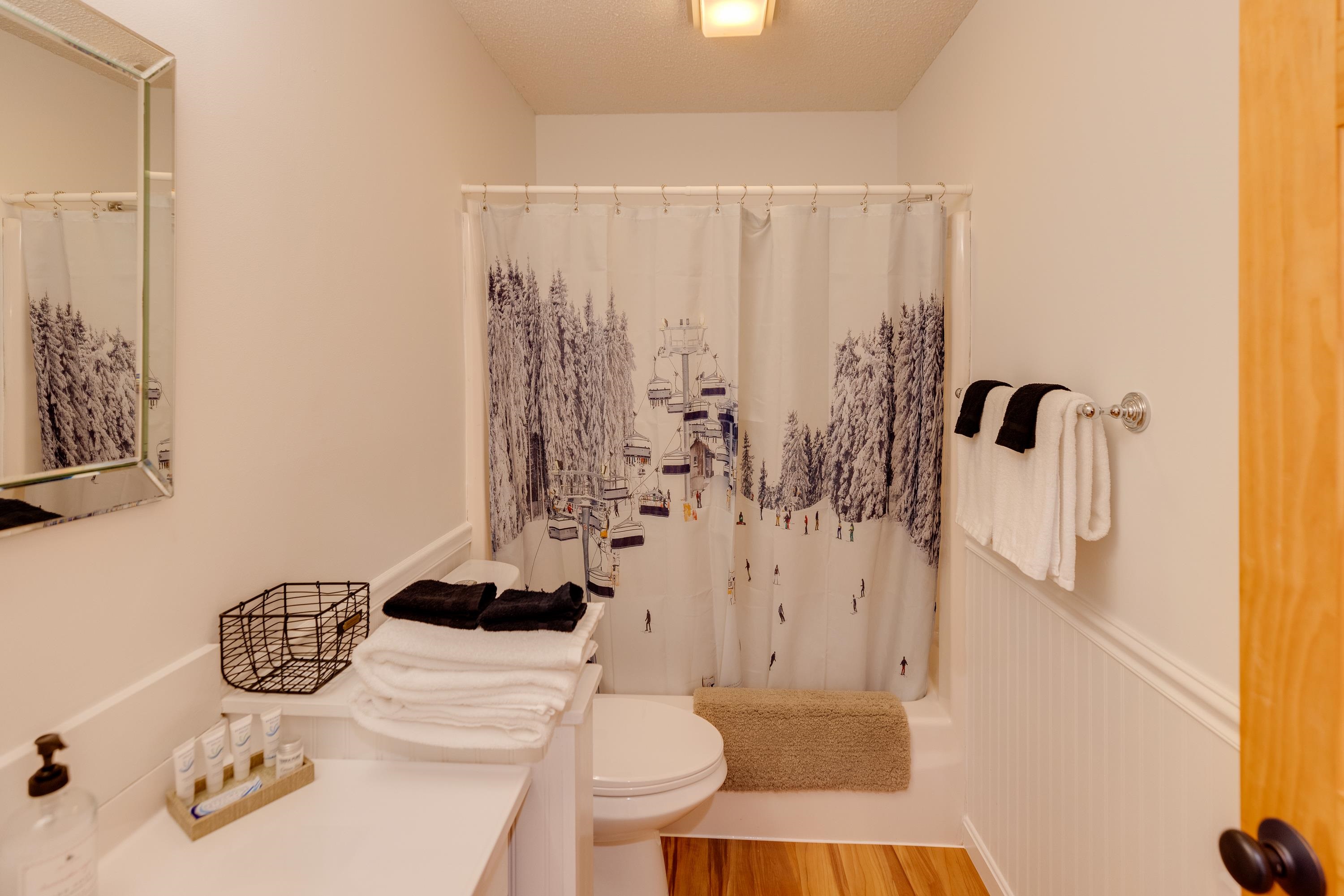 Bathroom with a ski-slope shower curtain, bathtub, toilet, and neatly stacked towels.
