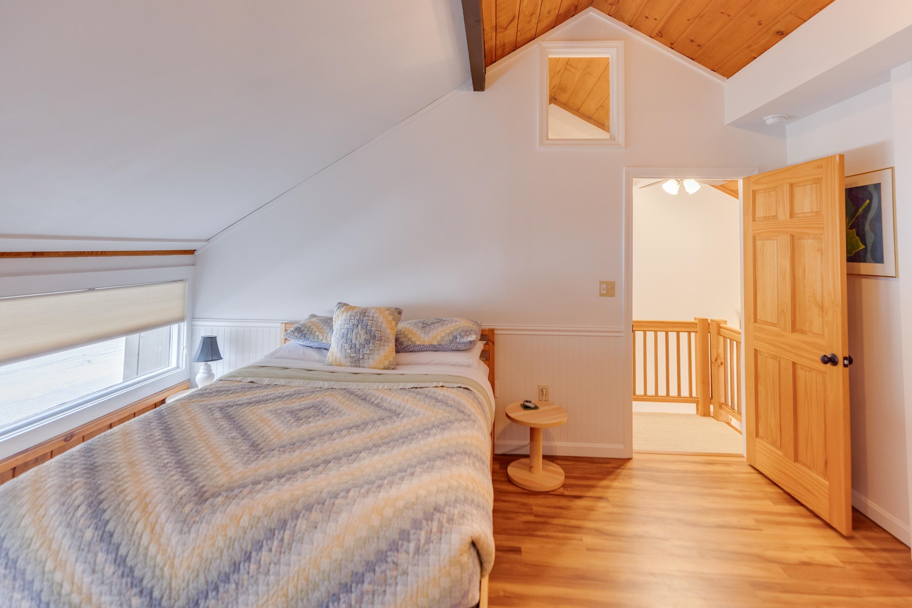 Attic bedroom with a bed under a sloped ceiling and a wooden door opening onto a landing.