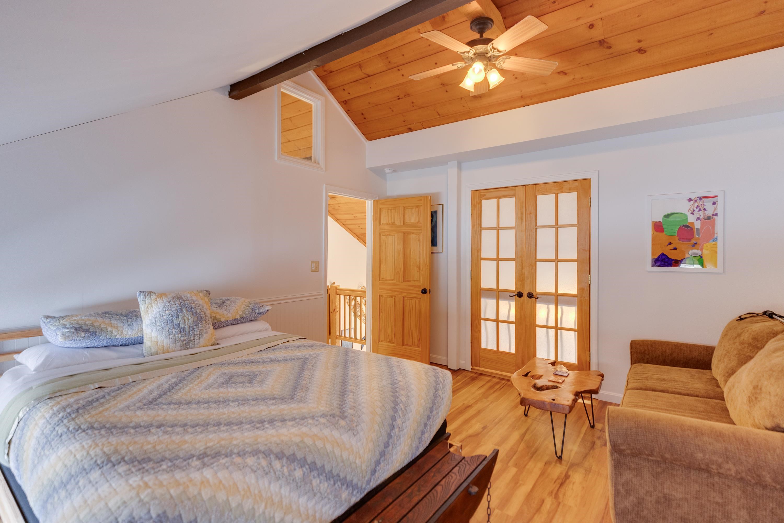 Bedroom with vaulted wood ceiling, large bed, brown sofa, and wooden French doors.