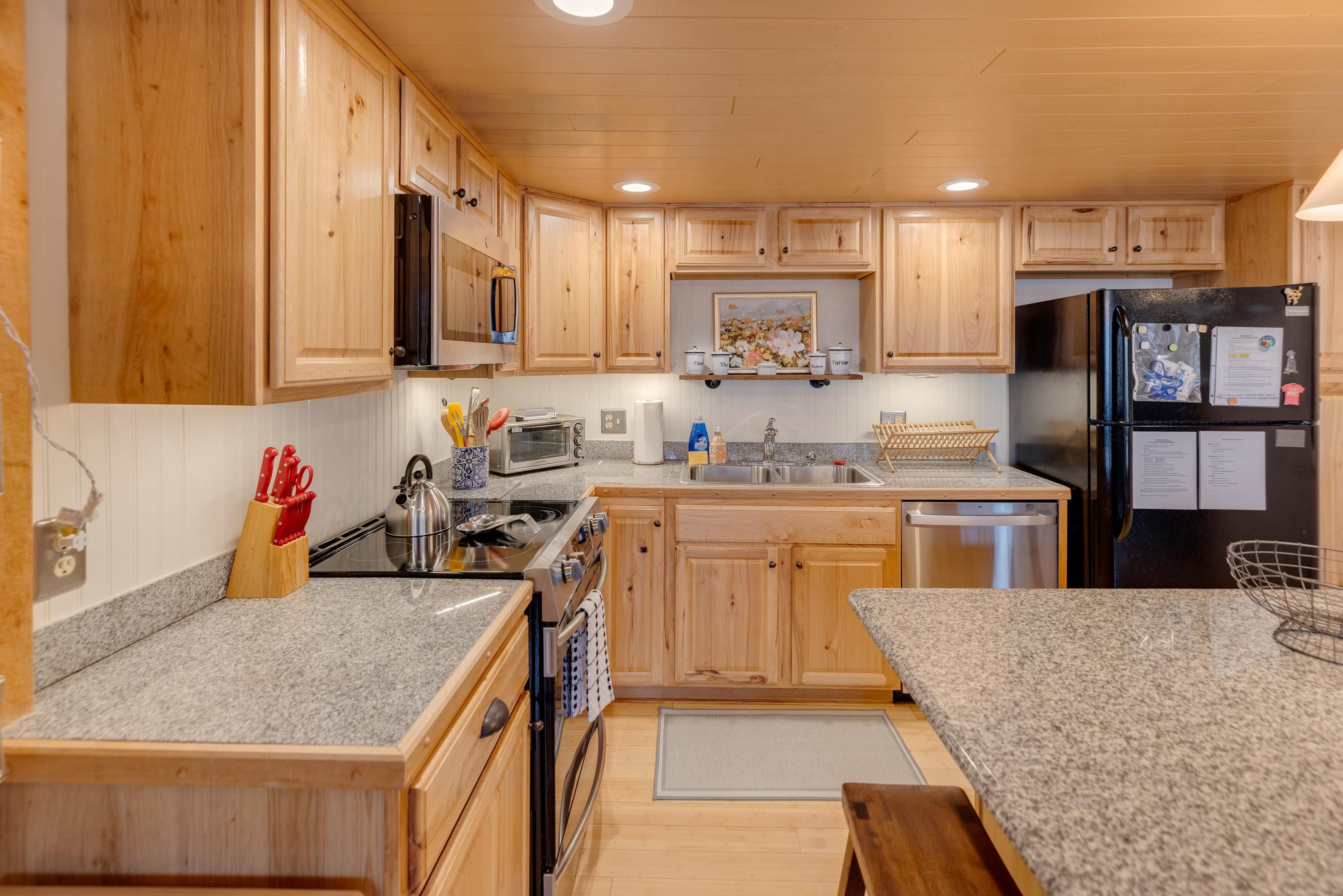 Kitchen with light wood cabinetry, granite counters, stainless steel appliances, and a black refrigerator.