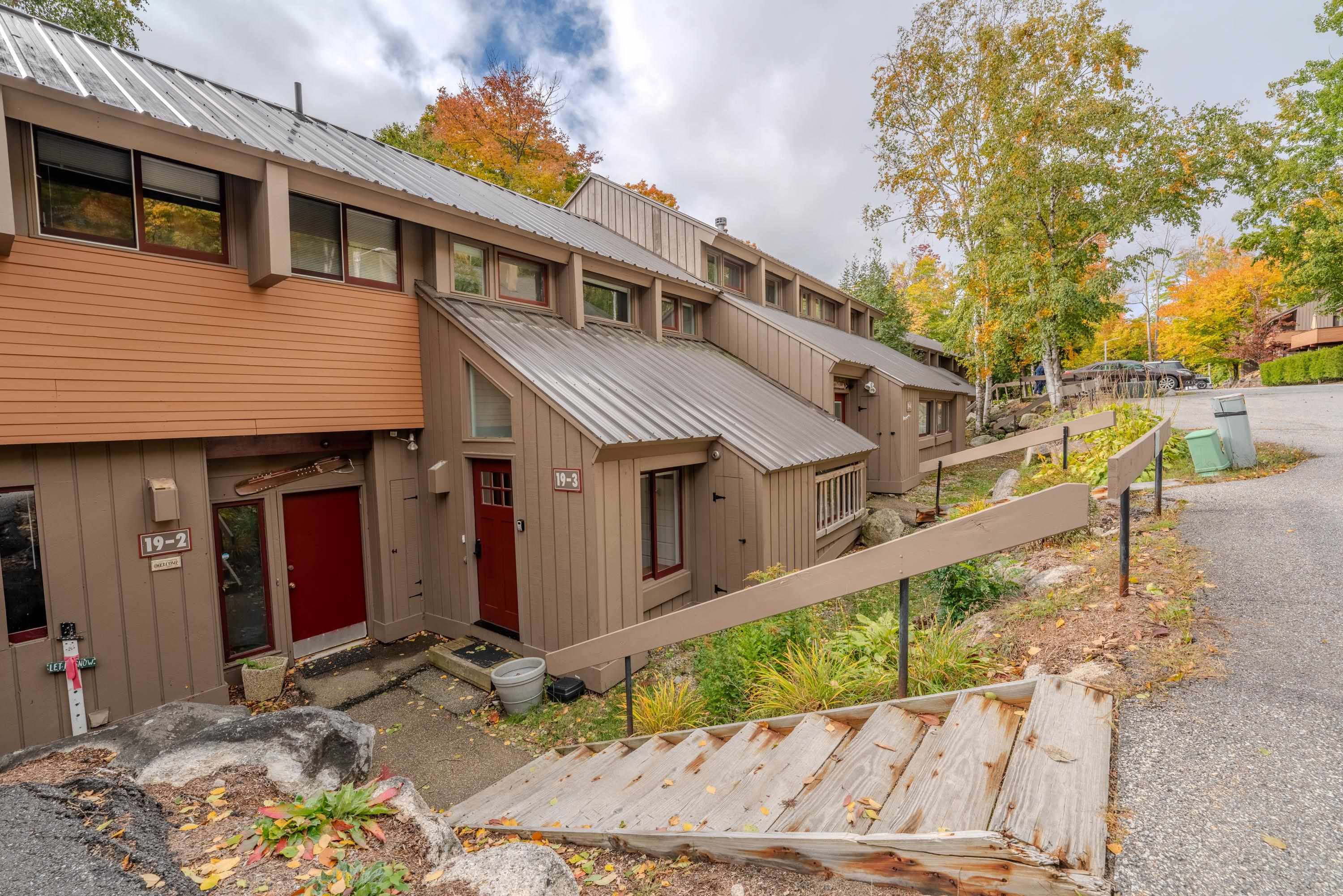 Townhome exterior with a red unit 3 door, sloped metal roof, and wooden access ramp.