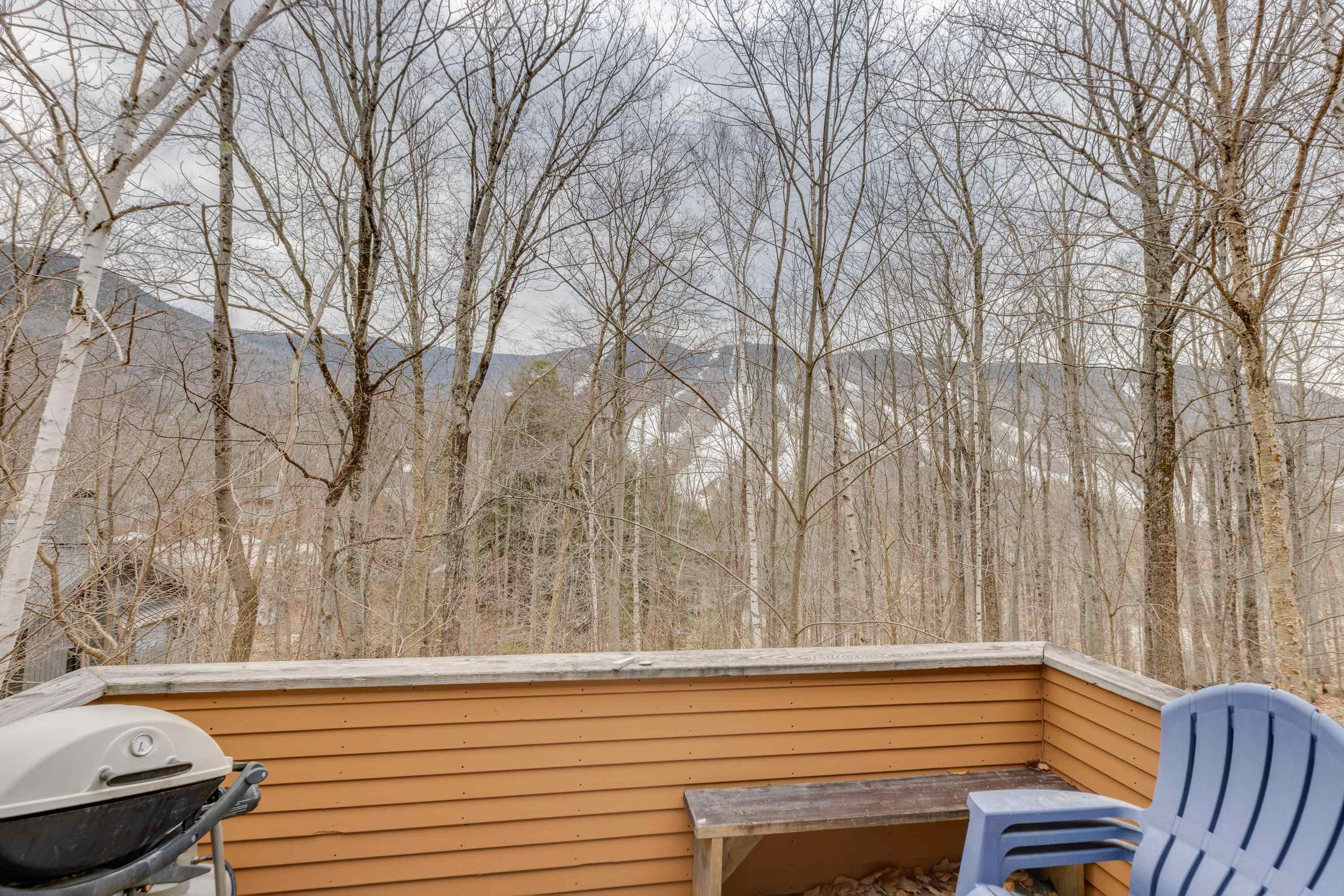 Deck with a grill and blue chair overlooking wooded mountain ridges.