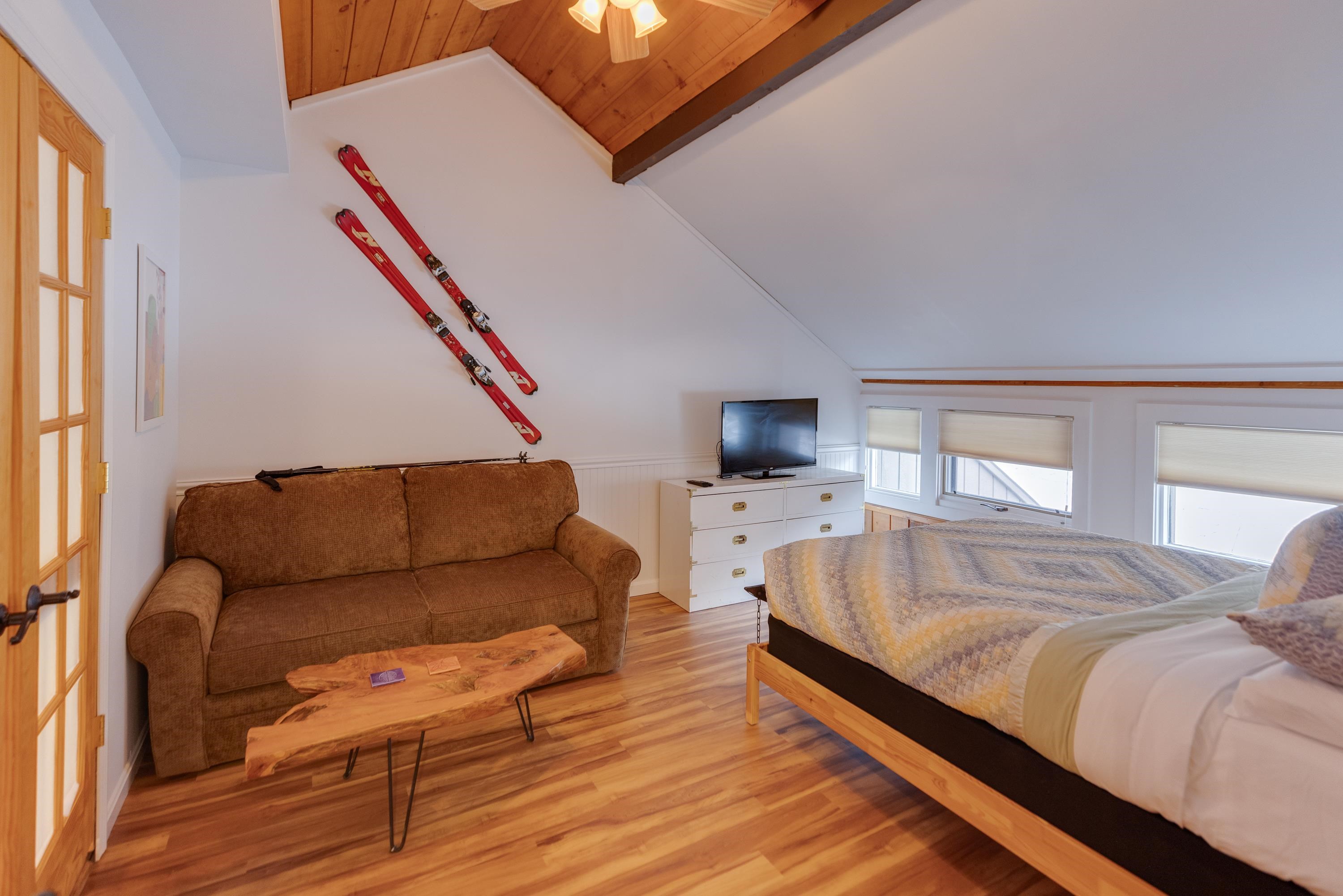 Bedroom with a vaulted wood ceiling, bed, sofa, and red skis mounted on the wall.