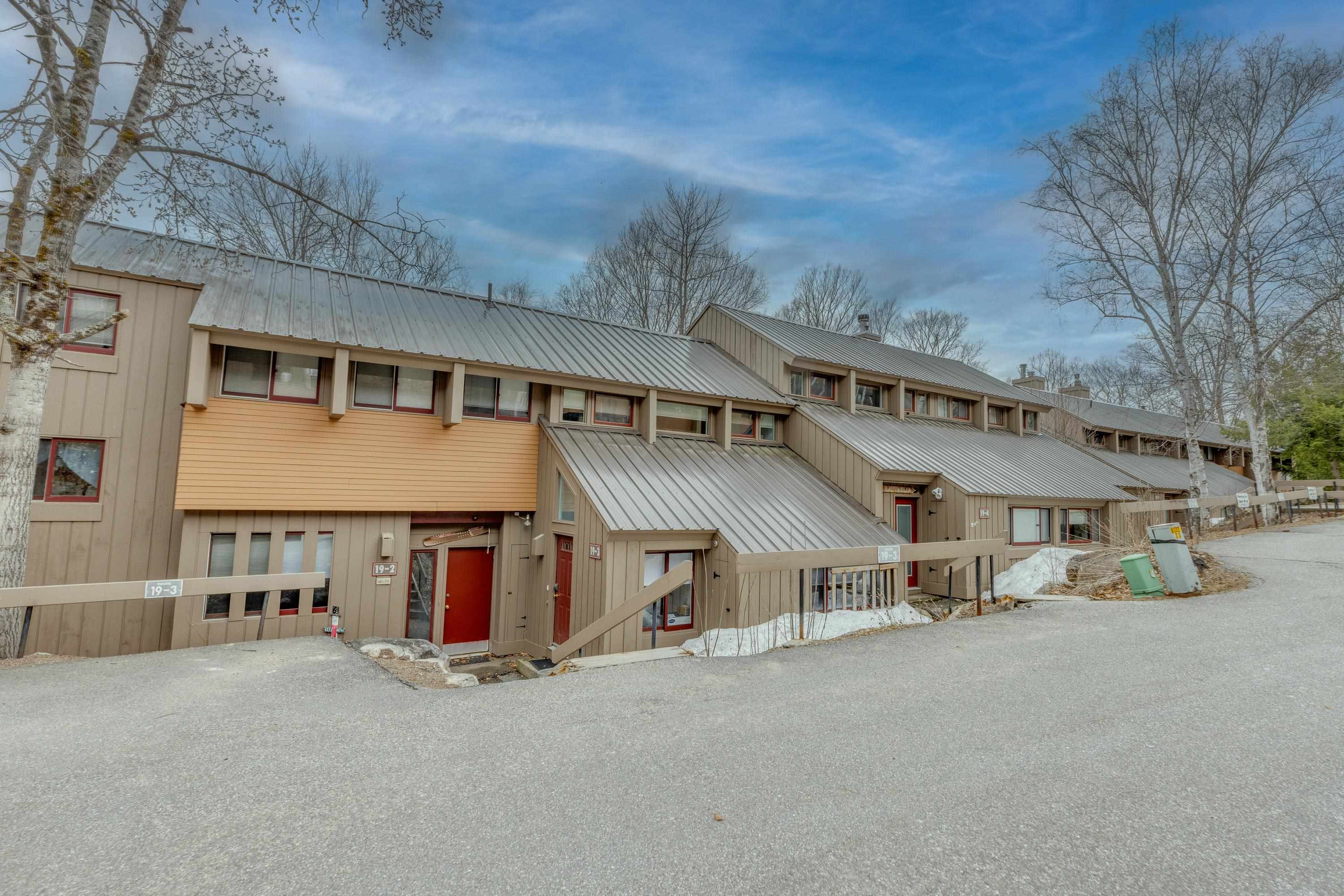 Condominium exterior with tan siding, metal roofs, red doors, and unit 19-3 signage.