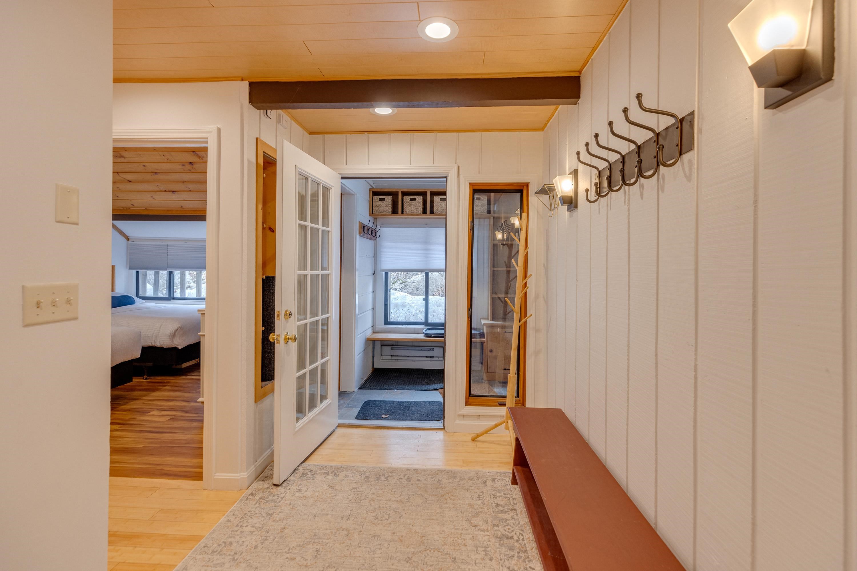 Entryway with a long bench and coat hooks, leading to a window seat overlooking snowy grounds.