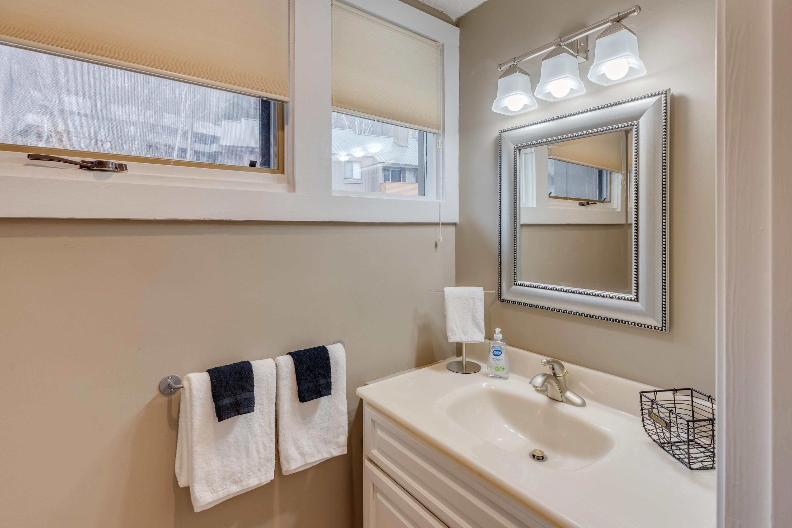 Bathroom vanity with a white sink, framed mirror, and windows with blinds.