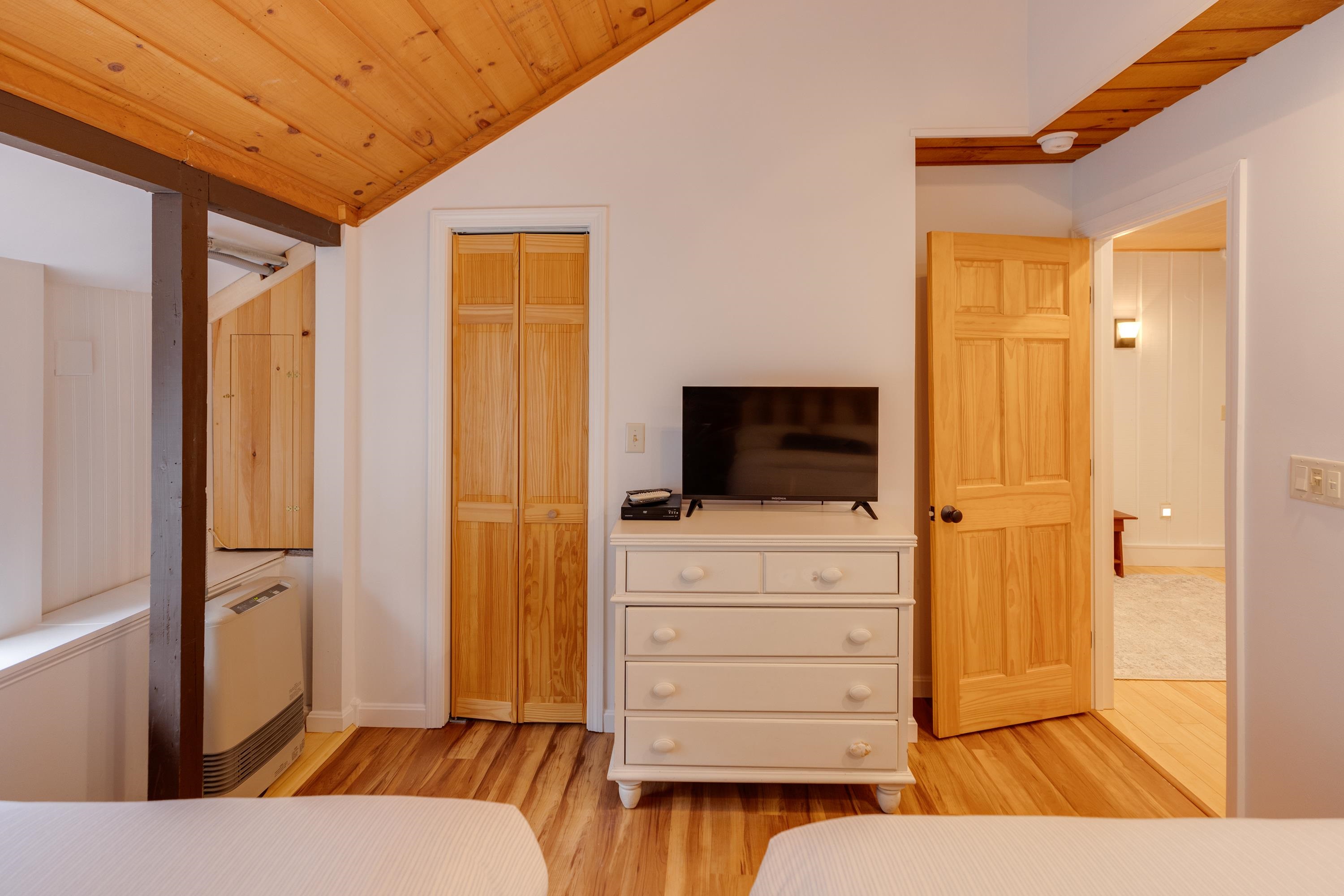 Bedroom with a sloped wood ceiling, twin beds, and a white dresser topped by a television.