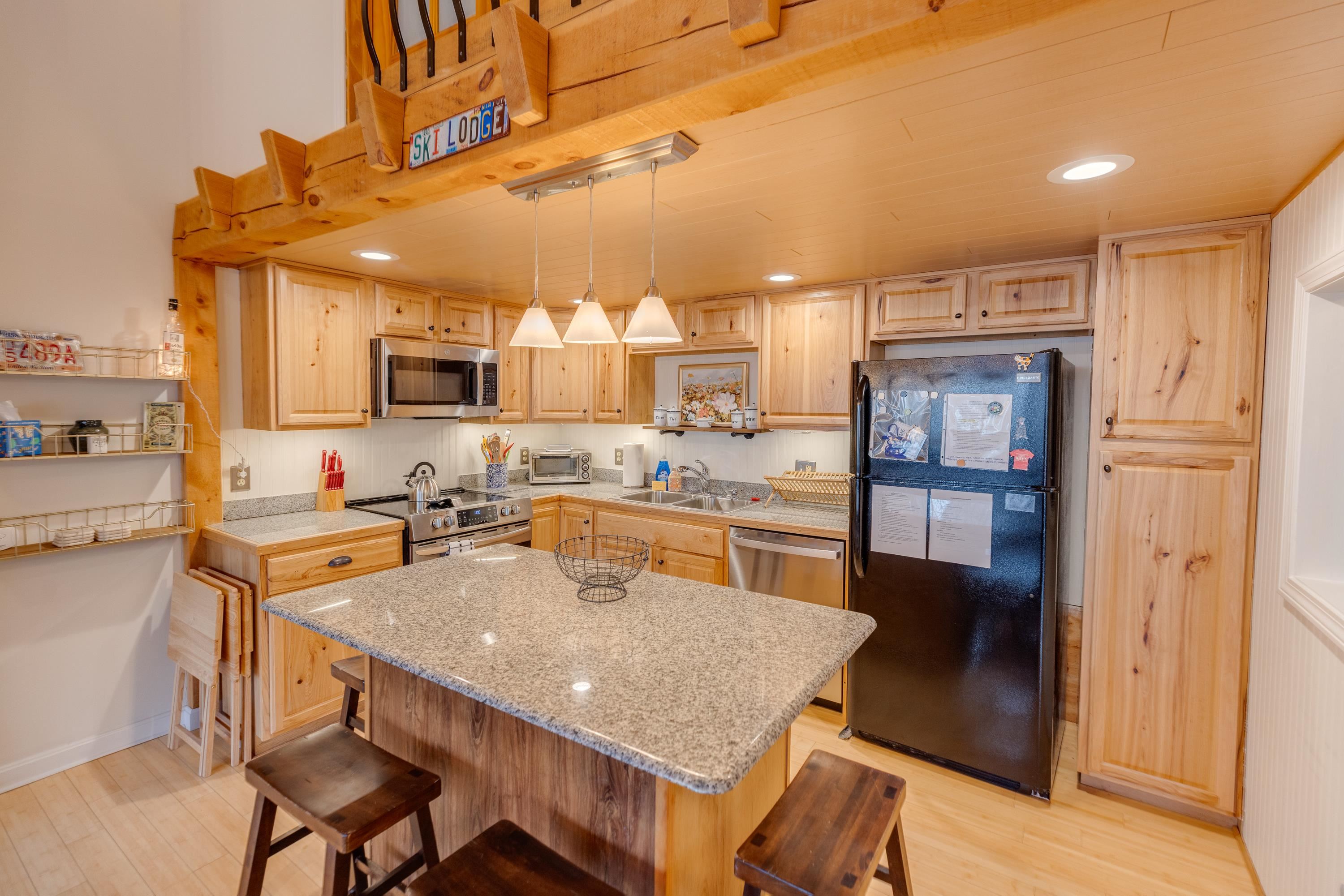 Kitchen with honey-toned wood cabinetry, granite island, pendant lights, and stainless steel appliances.
