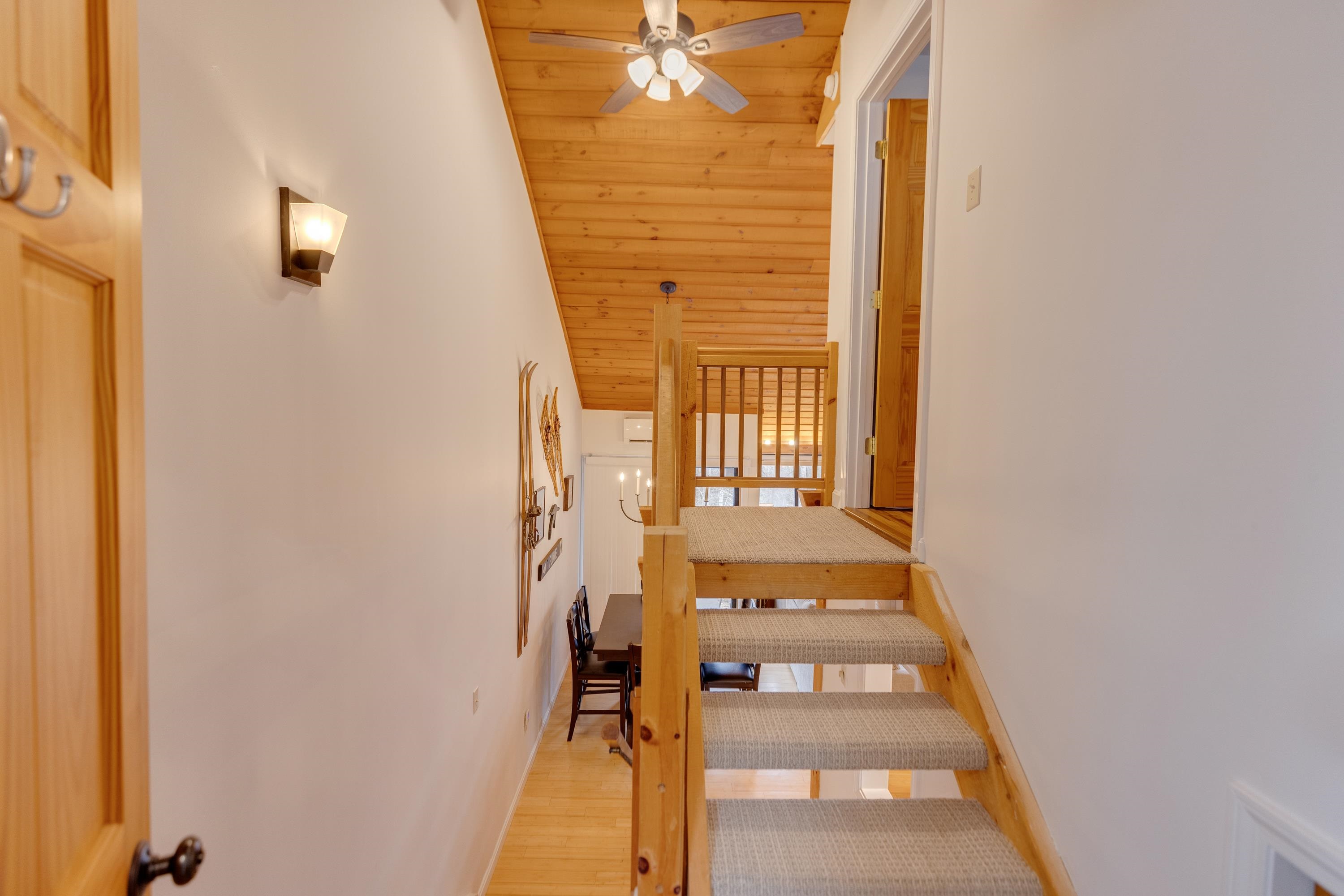 Open-riser wooden staircase with carpeted treads leads to a landing beneath a sloped wood ceiling.