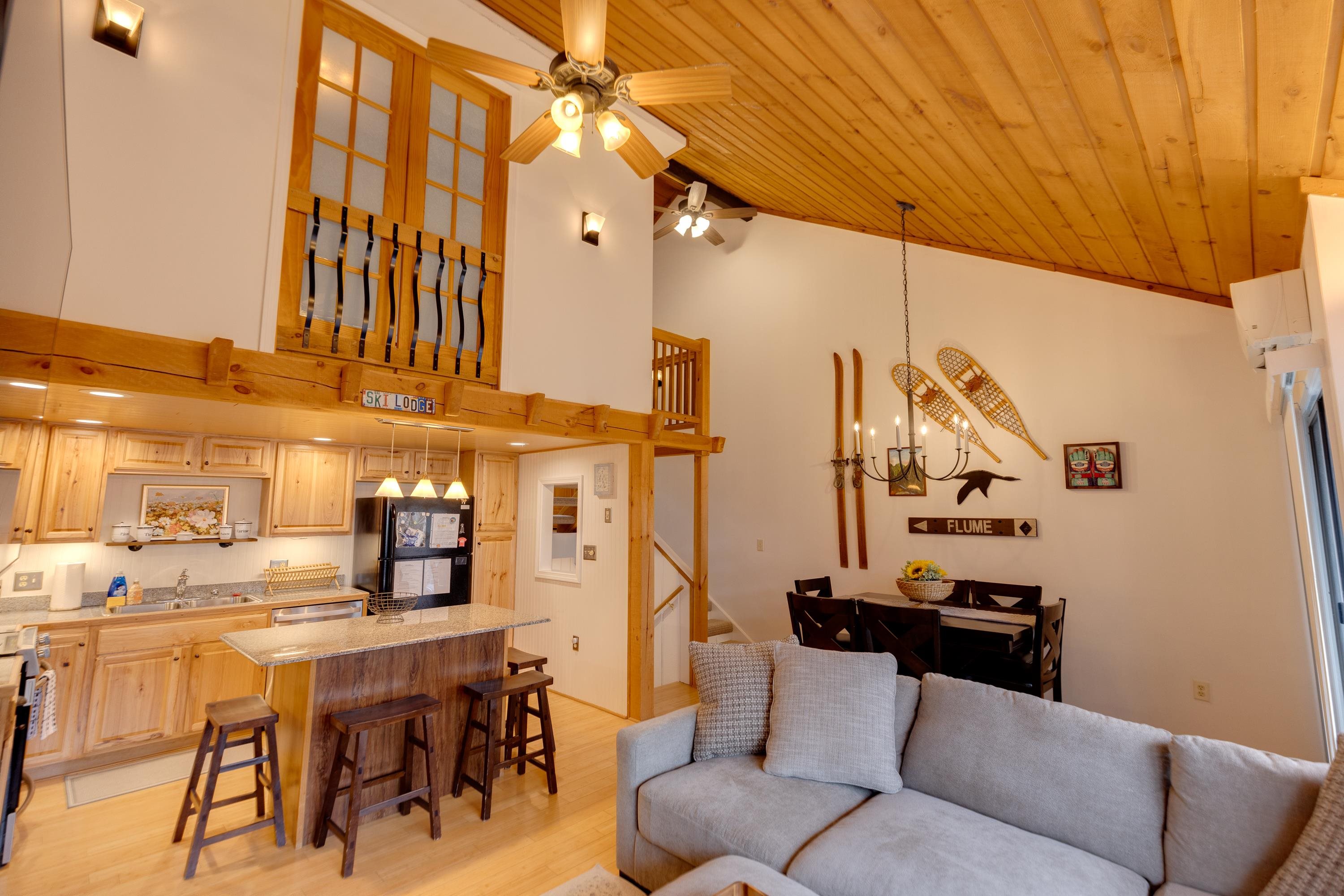 Open-concept living area with a kitchen island, loft, vaulted wood ceiling, and ski-themed decor.