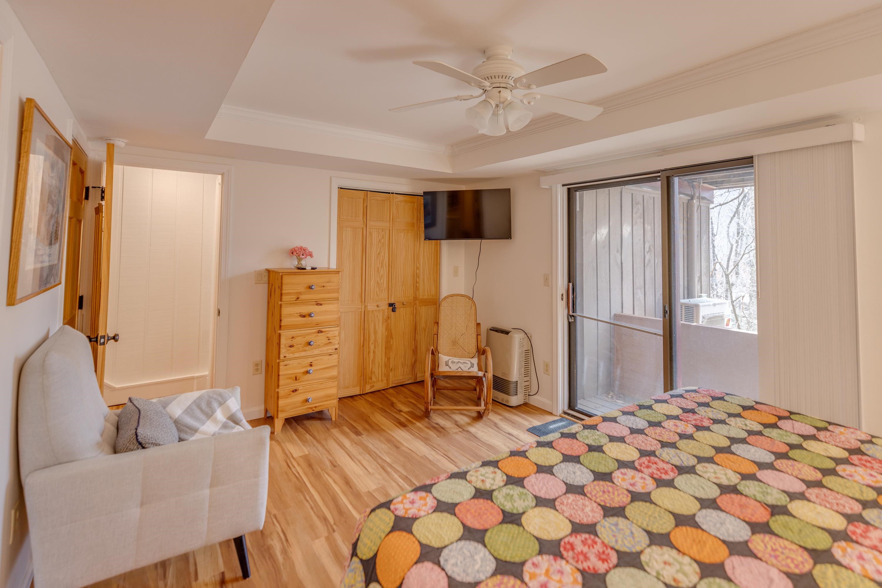Bedroom with a colorful patchwork quilt, wood floors, and sliding glass doors overlooking a snowy balcony.