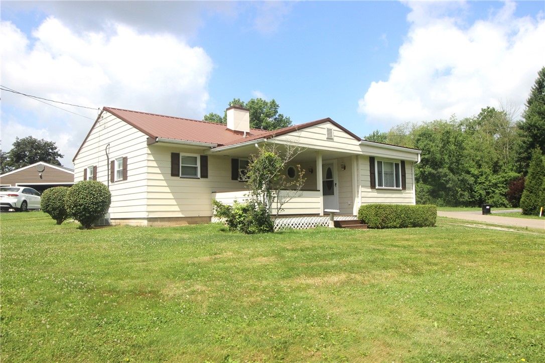 Cream single-story house with a red metal roof, covered porch, and broad lawn.