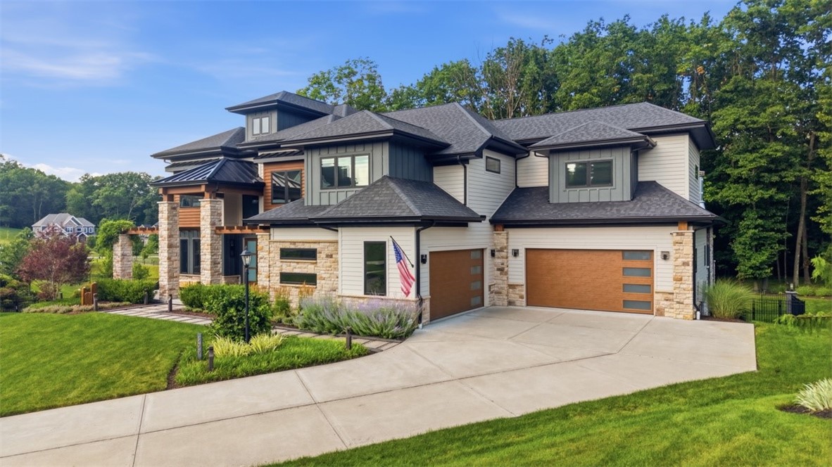 Modern two-story home with stone accents, wood-tone garage doors, and a landscaped curved driveway.