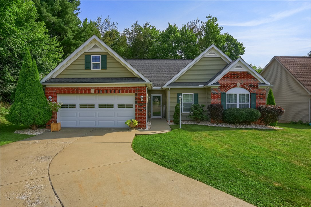 Single-story home with red brick accents, green siding, a two-car garage, and curved driveway.
