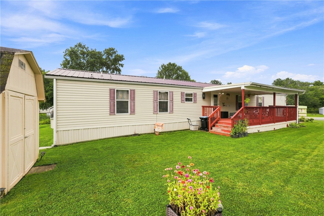 Manufactured home with a covered porch, red railings, and a wide green lawn.