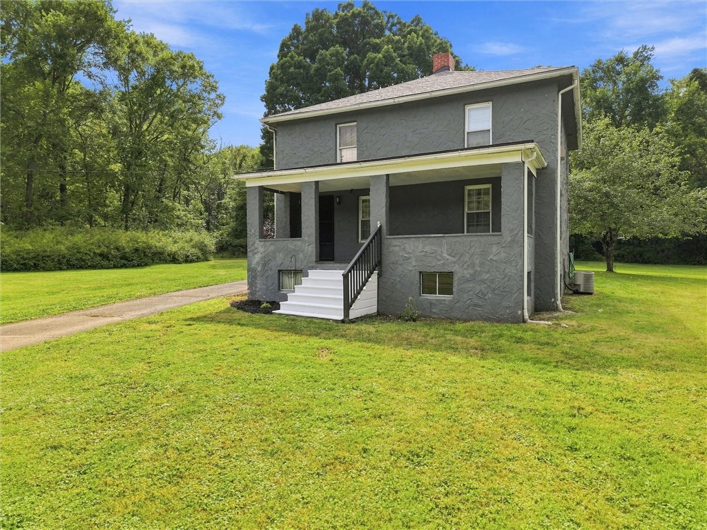 Gray two-story house with a covered porch and white steps, surrounded by a broad lawn and mature trees.
