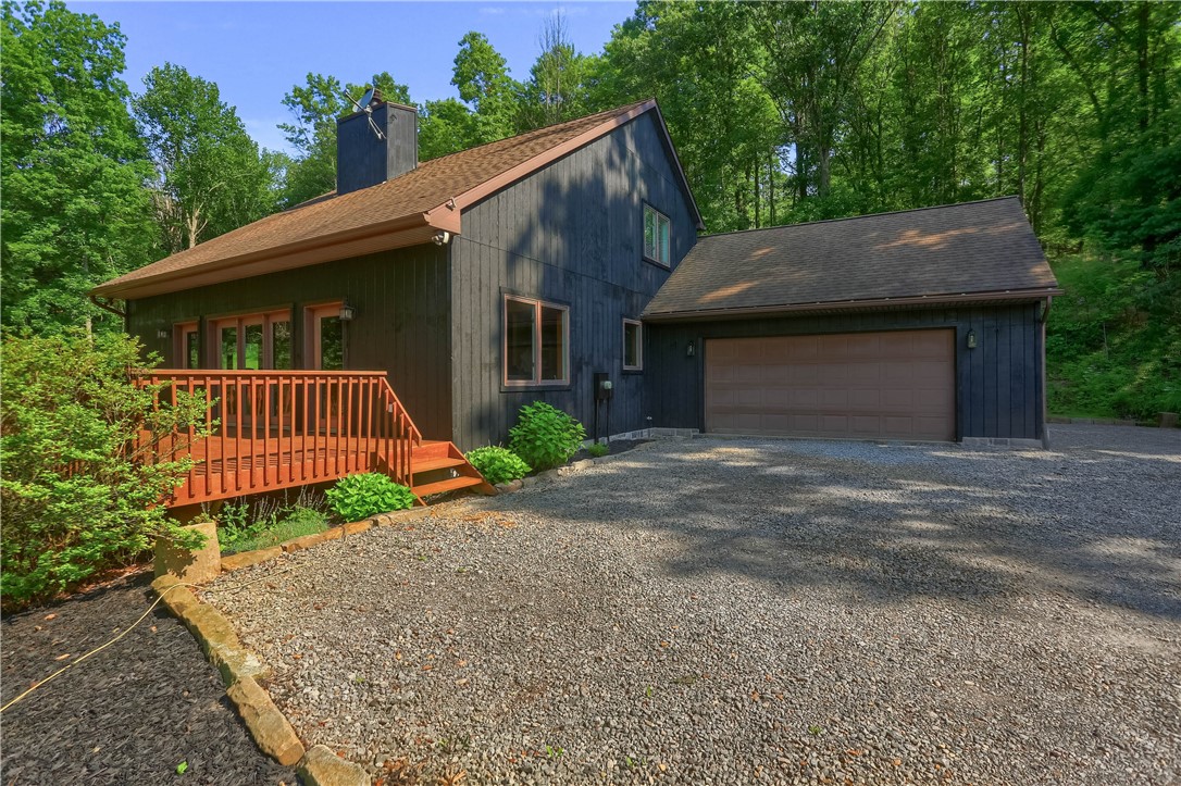 Dark-sided house with a raised wooden deck, gravel driveway, and attached garage.