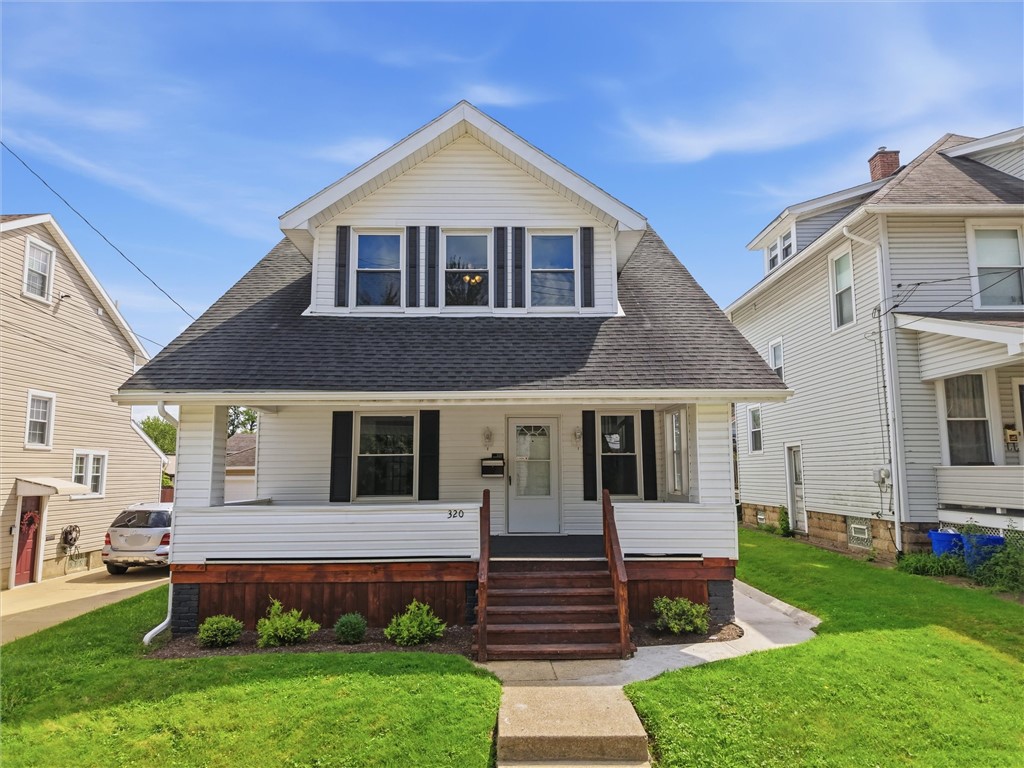 White two-story house with a large dormer, covered porch, and green front lawn.