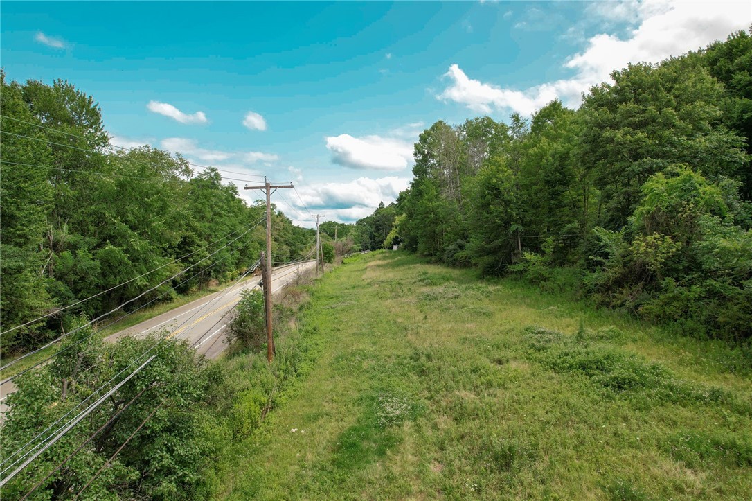 Vacant grassy lot bordered by woods, with a road and utility poles along one side.