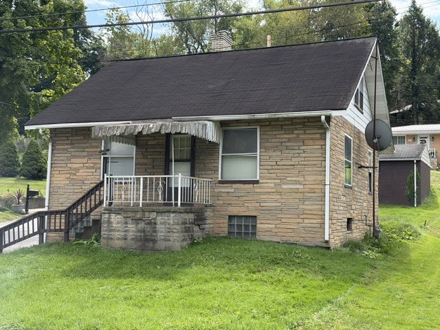One-story stone house with a covered porch and dark pitched roof on a grassy lot.
