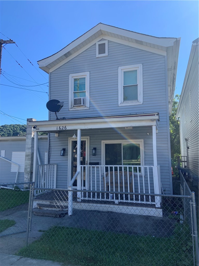 Two-story blue-gray house with a covered porch and chain-link fence.