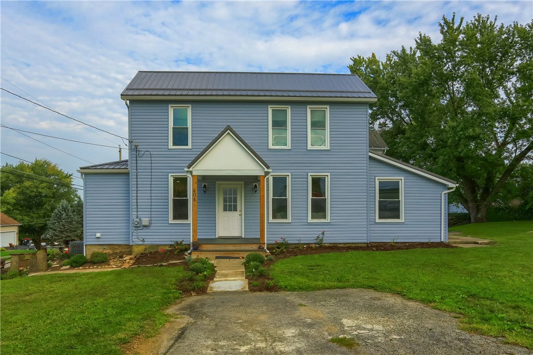 Two-story blue house with a metal roof, covered front entry, and lawn.