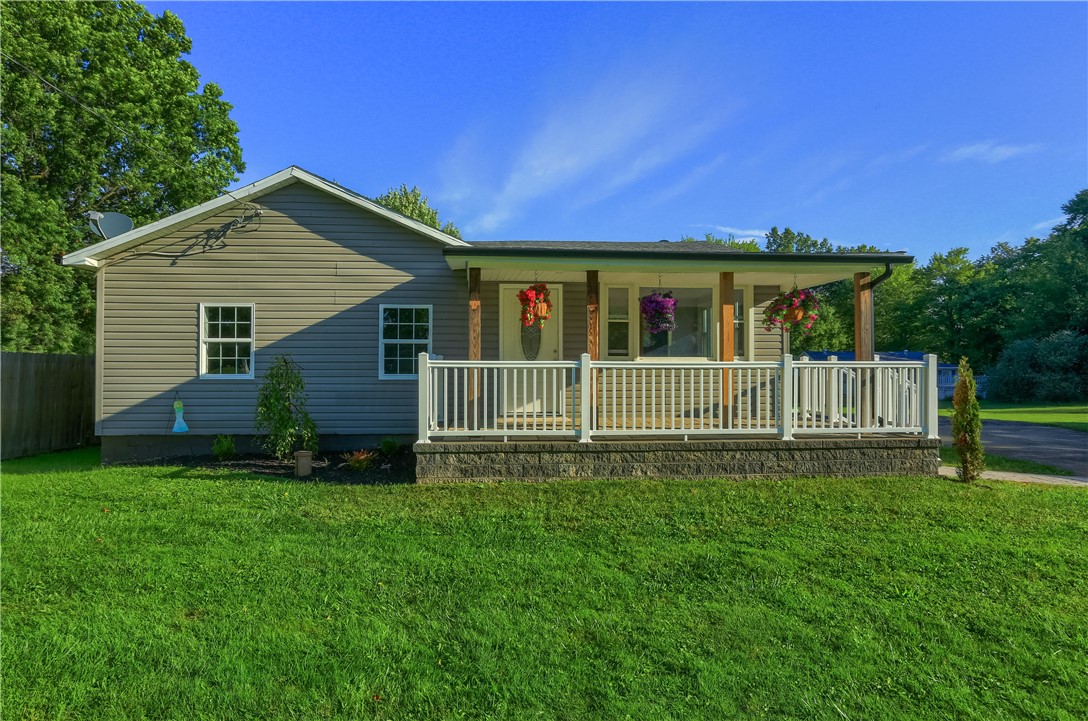 Single-story home with a covered porch, white railings, hanging flowers, and a broad green lawn.
