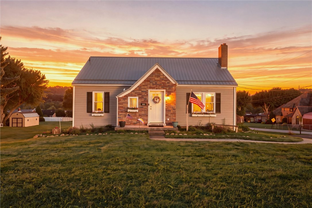 House with a stone entry and metal roof at sunset, set behind a broad lawn.