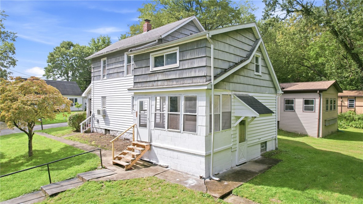 Two-story gray and white house with an enclosed porch, wooden steps, and a green lawn.