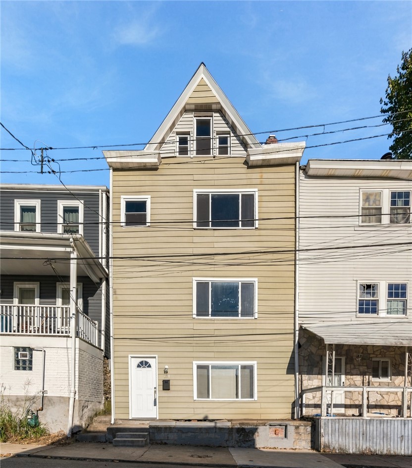 Narrow tan multi-story house with a tall pointed gable and white trim