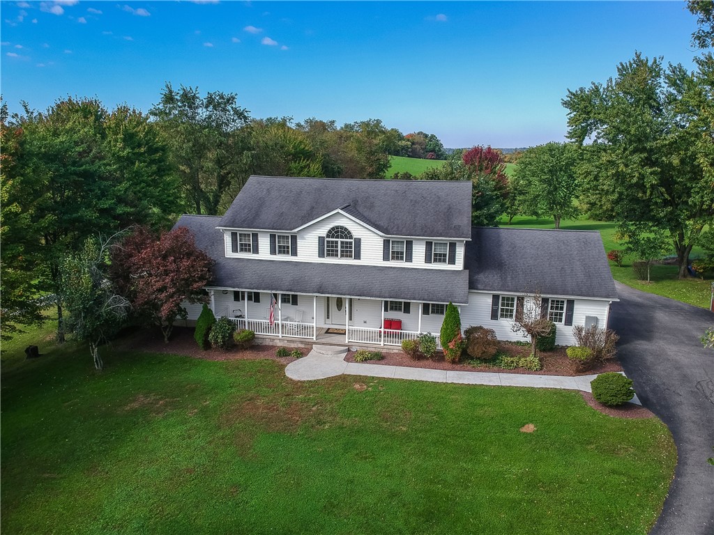 White two-story house with a covered porch, broad lawn, mature trees, and a curved driveway.