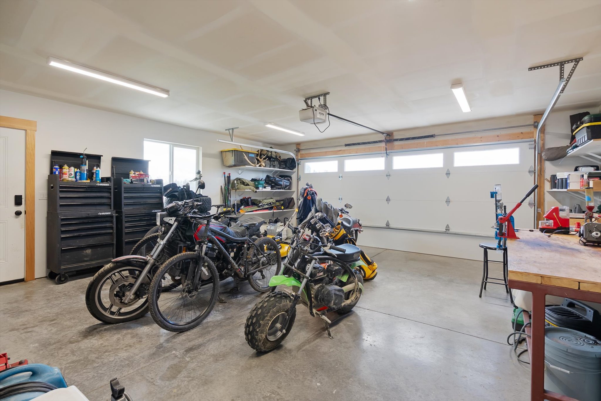 Garage with motorcycles, dirt bikes, black tool chests, and a workbench.