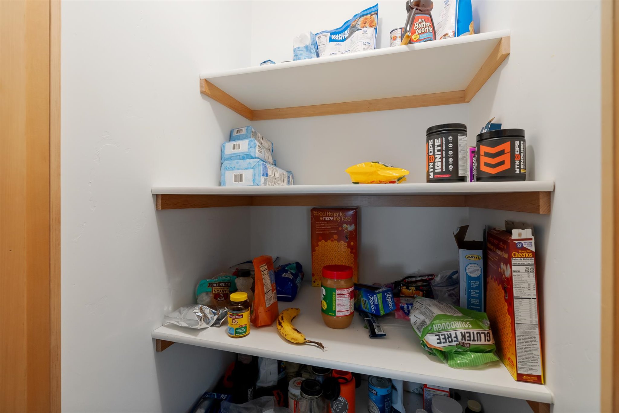 Stocked pantry with white shelves and wood trim, including cereal boxes, snacks, and groceries.