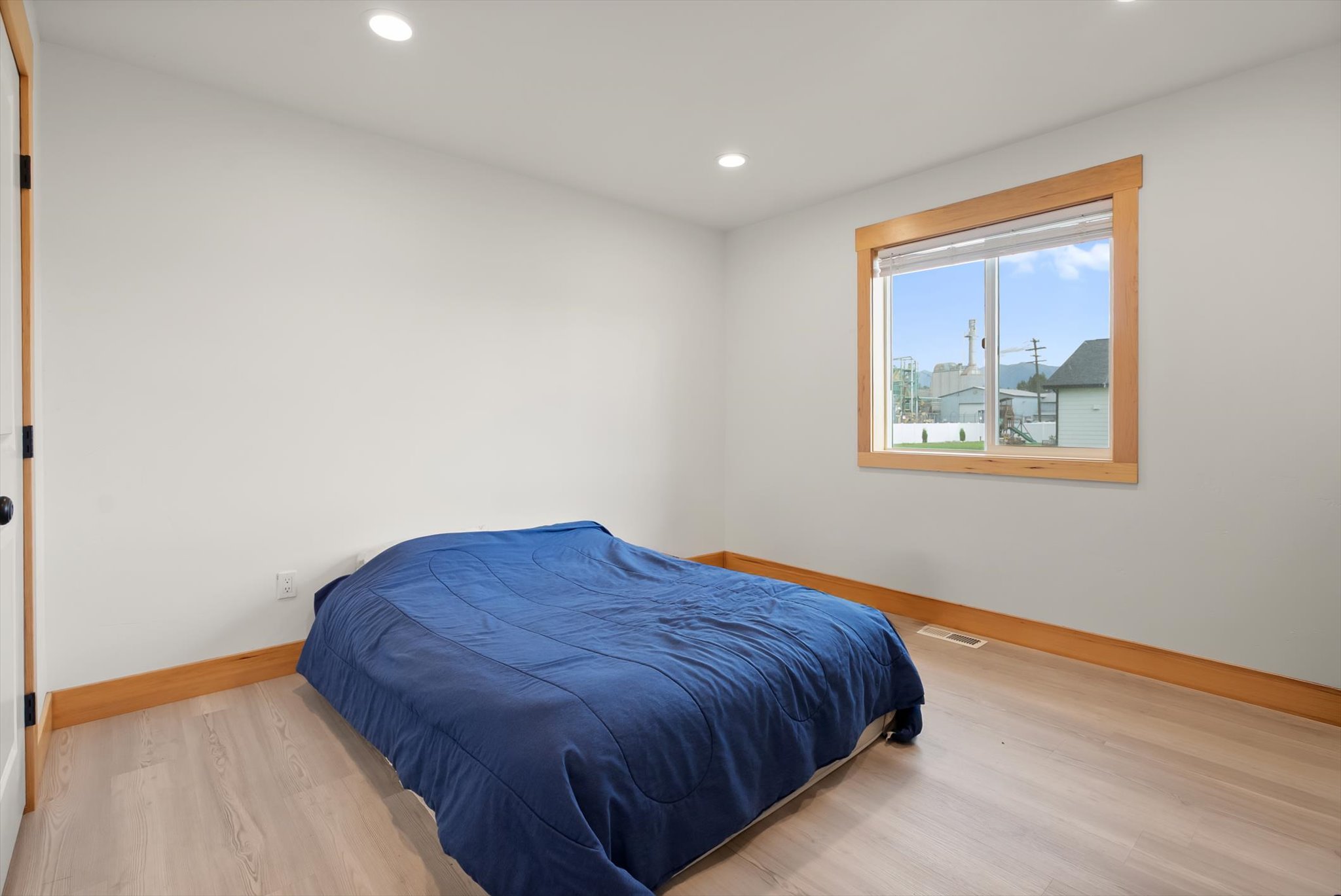 Bedroom with a low bed under a blue comforter and a window overlooking nearby buildings and mountains.