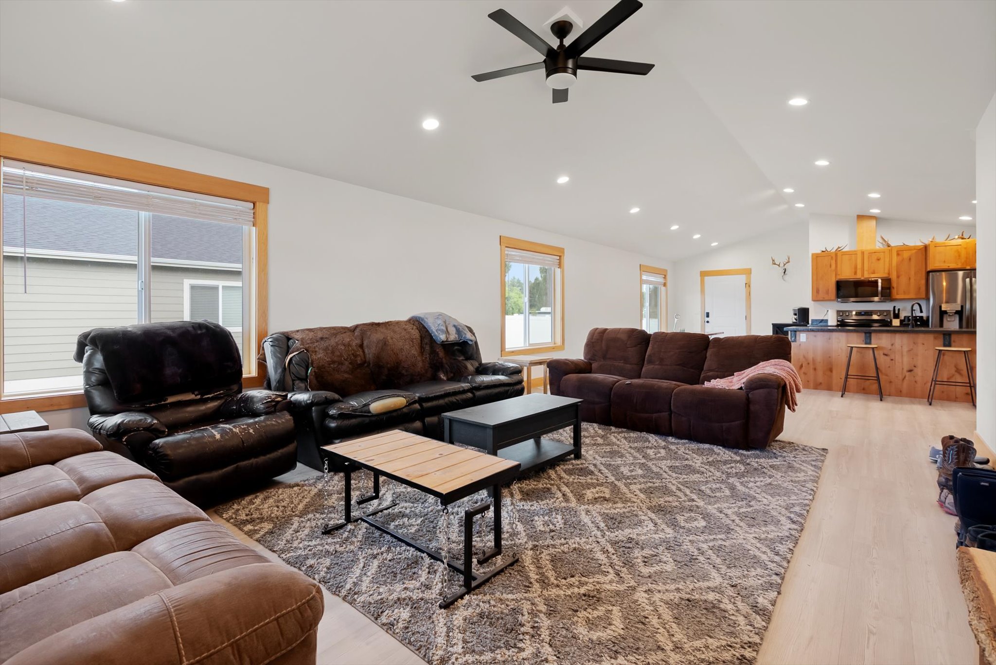 Open-plan living room with several sofas and a rug leading into a kitchen with wood cabinets and stainless appliances.