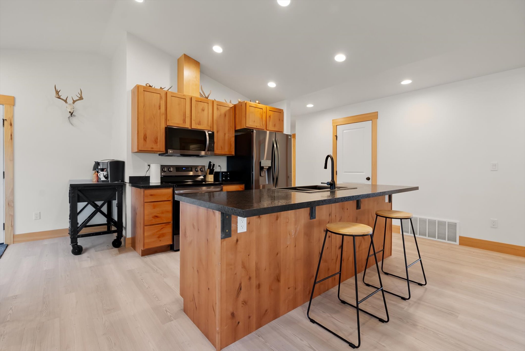 Kitchen with a large wood-paneled island, dark countertop, two stools, and stainless steel appliances.