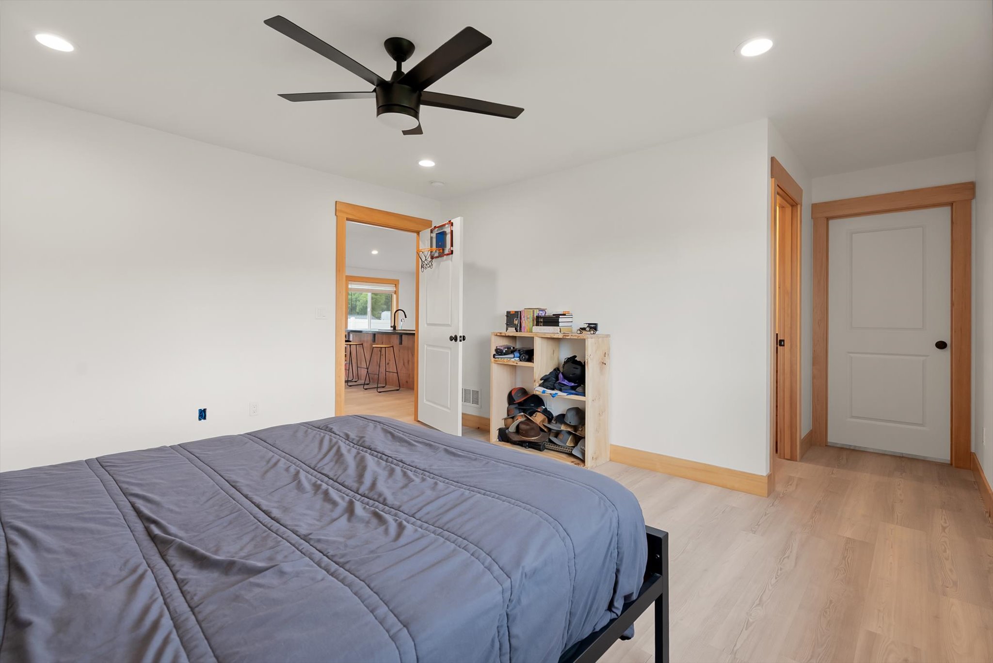 Bedroom with a gray-blue bed, black ceiling fan, and an open shelf displaying helmets.