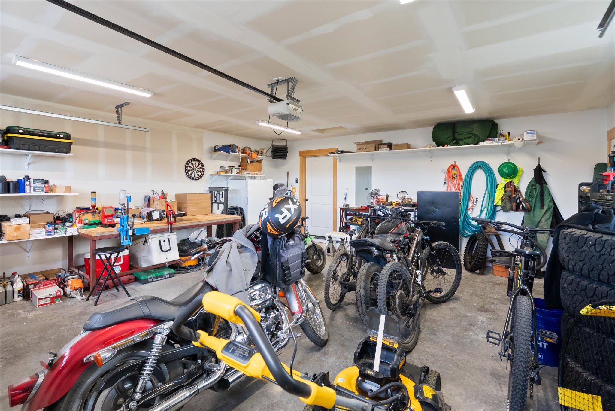 Garage packed with motorcycles and bicycles, with a workbench and storage shelves along the walls.