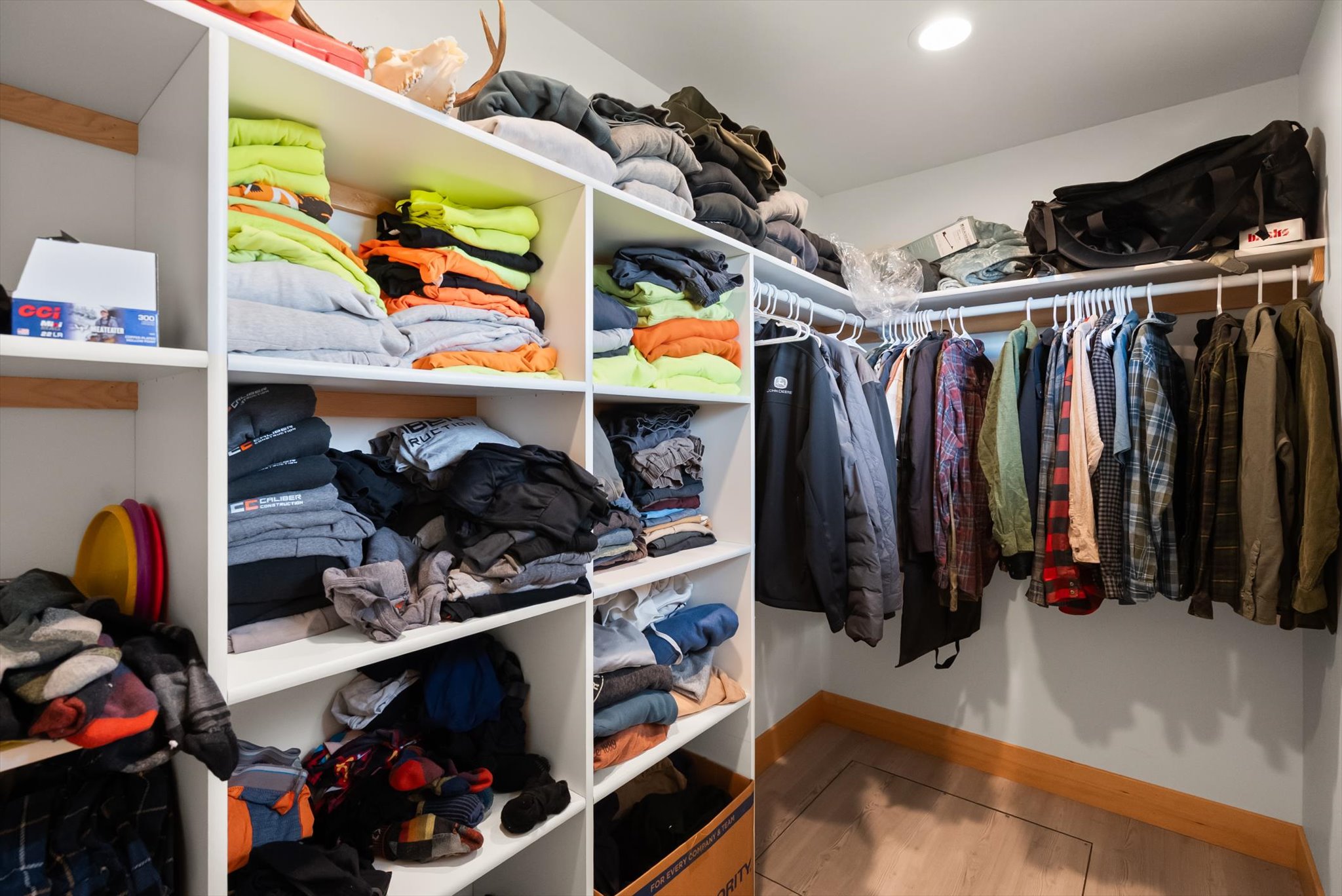 Walk-in closet with built-in shelves of folded clothes and a rod of hanging jackets and shirts.