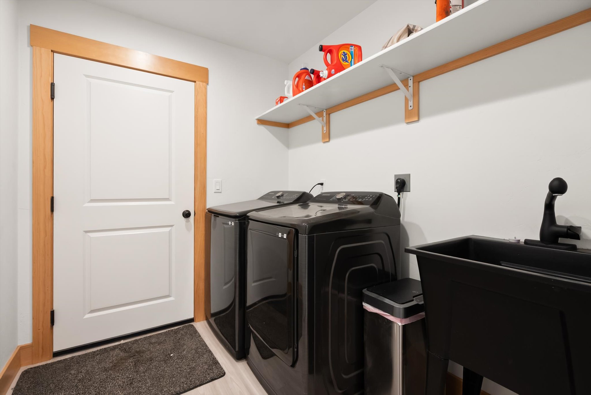 Laundry room with black washer and dryer beside a deep utility sink and wall shelves.
