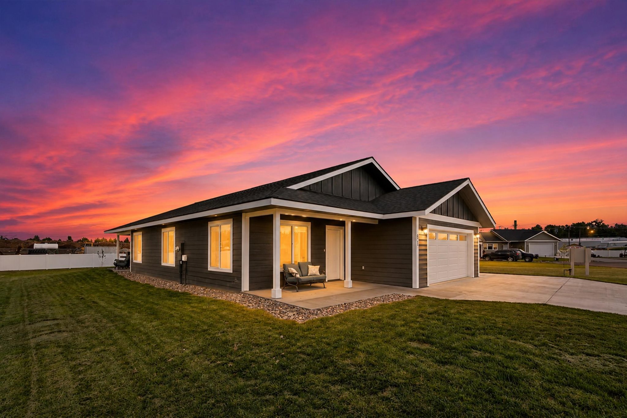 Modern dark-sided home with a covered porch and garage beneath a vivid sunset sky.