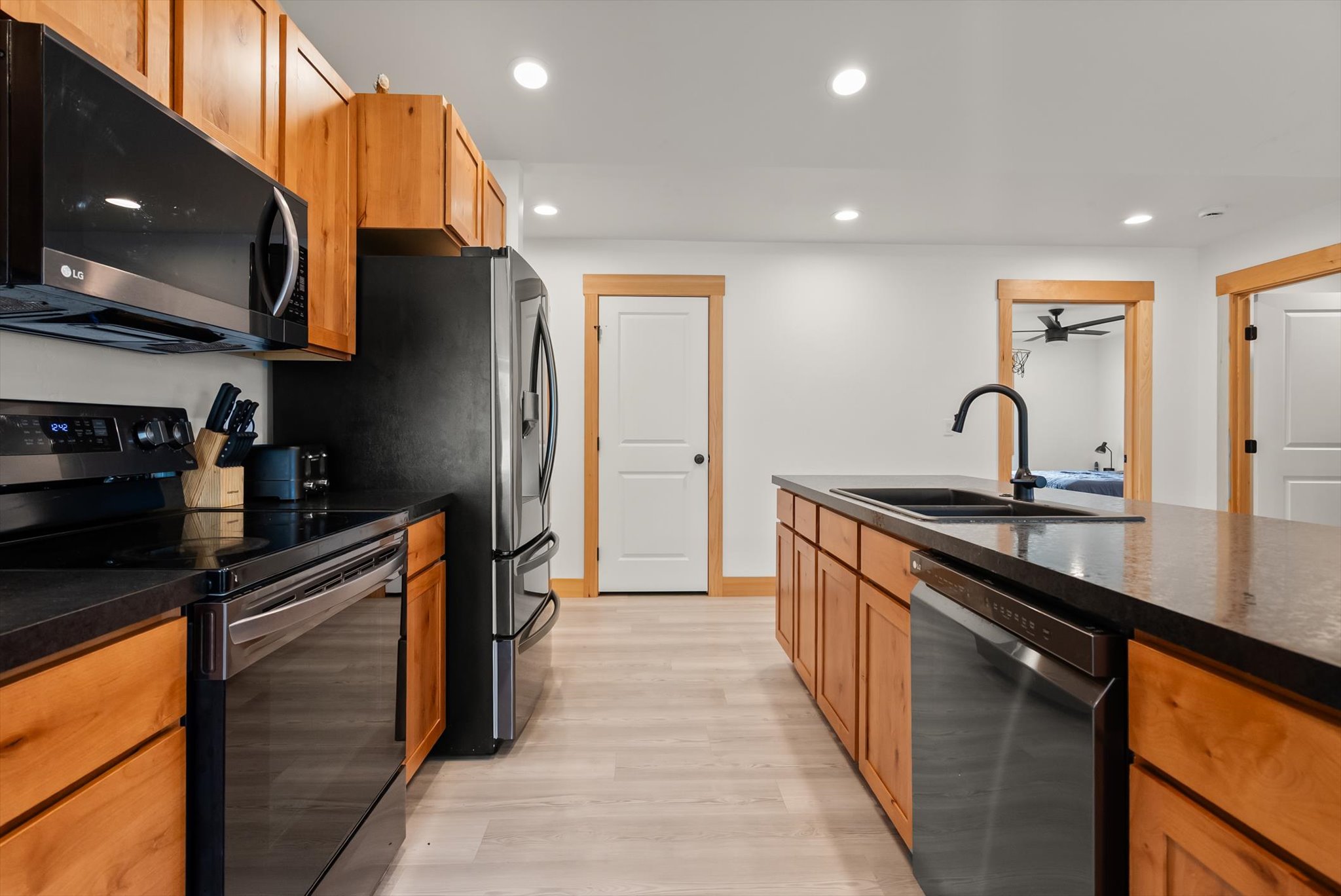 Kitchen with warm wood cabinets, dark counters, black appliances, and a long island sink.