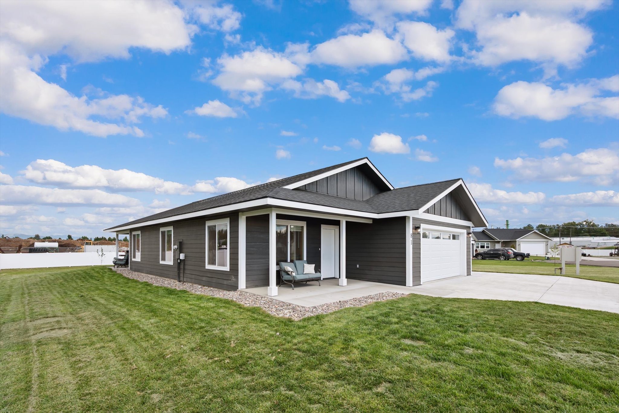 Single-story dark gray home with a covered porch, white garage door, and broad green lawn.