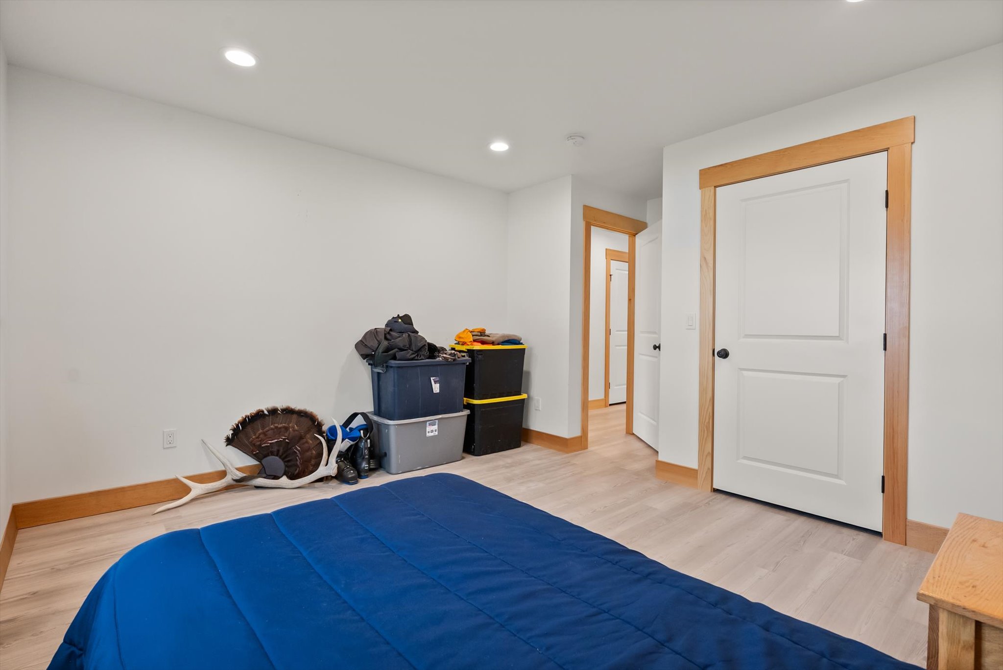 Bedroom with a blue bedspread, stacked storage bins, and light wood trim.