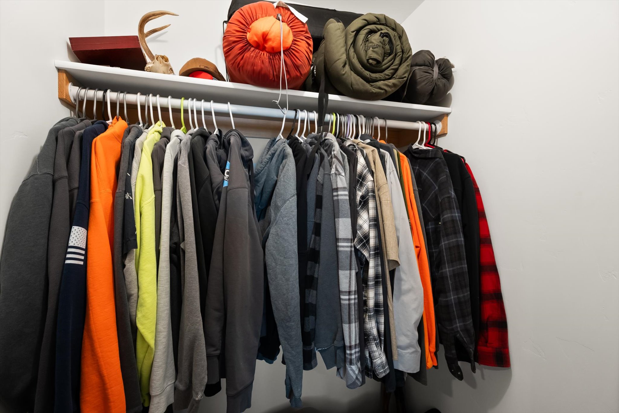 Closet packed with hanging clothes, with rolled sleeping bags and gear on the shelf above.