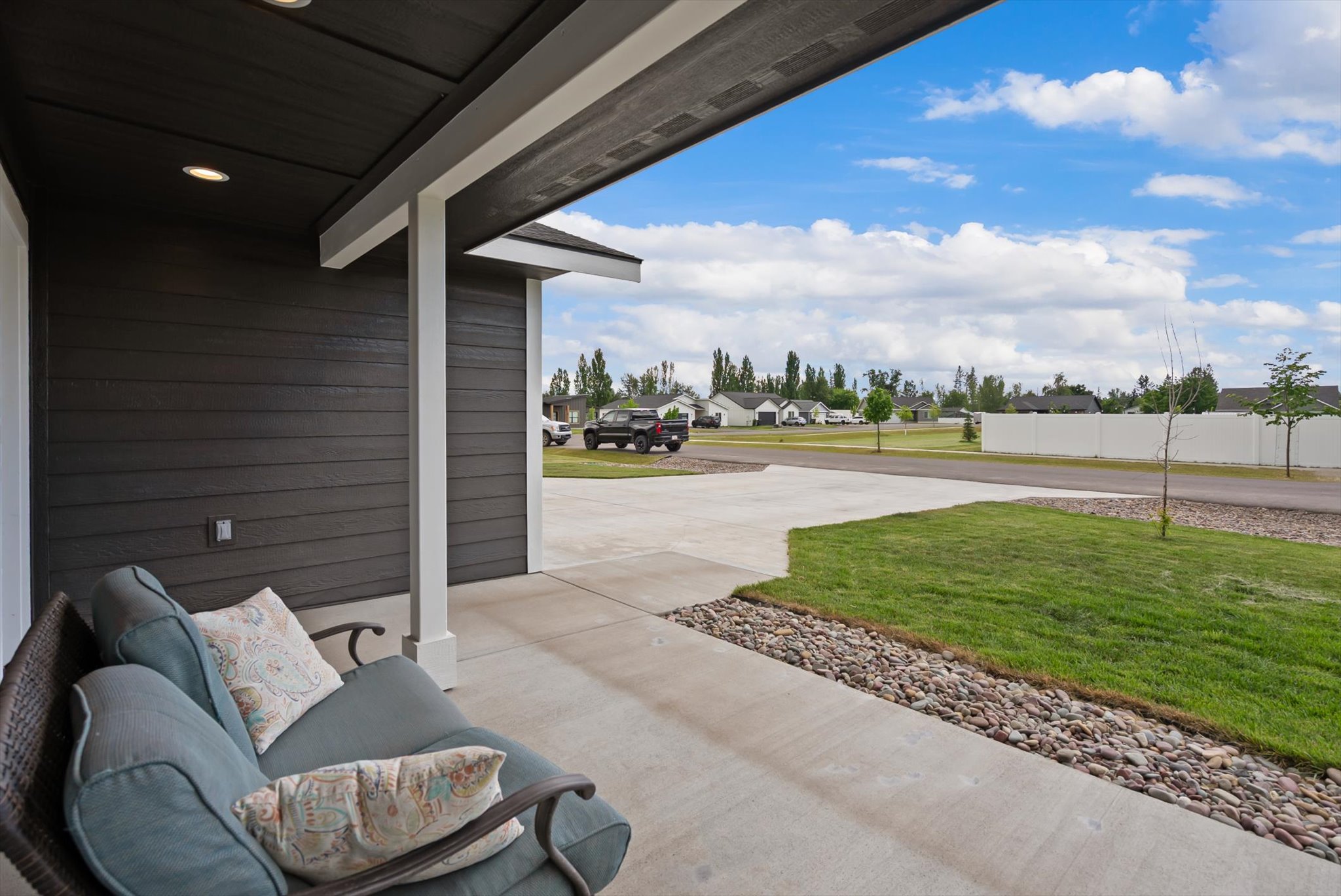 Covered patio with a cushioned loveseat overlooking the lawn, driveway, and neighboring homes.