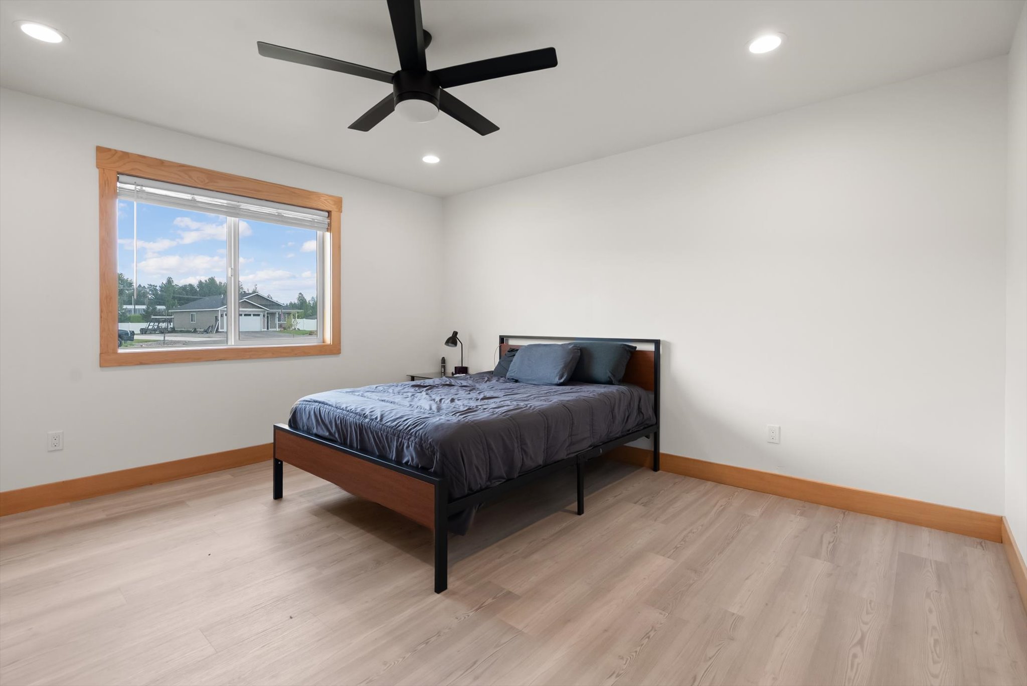 Bedroom with a dark gray bed, black ceiling fan, and large wood-trimmed window.