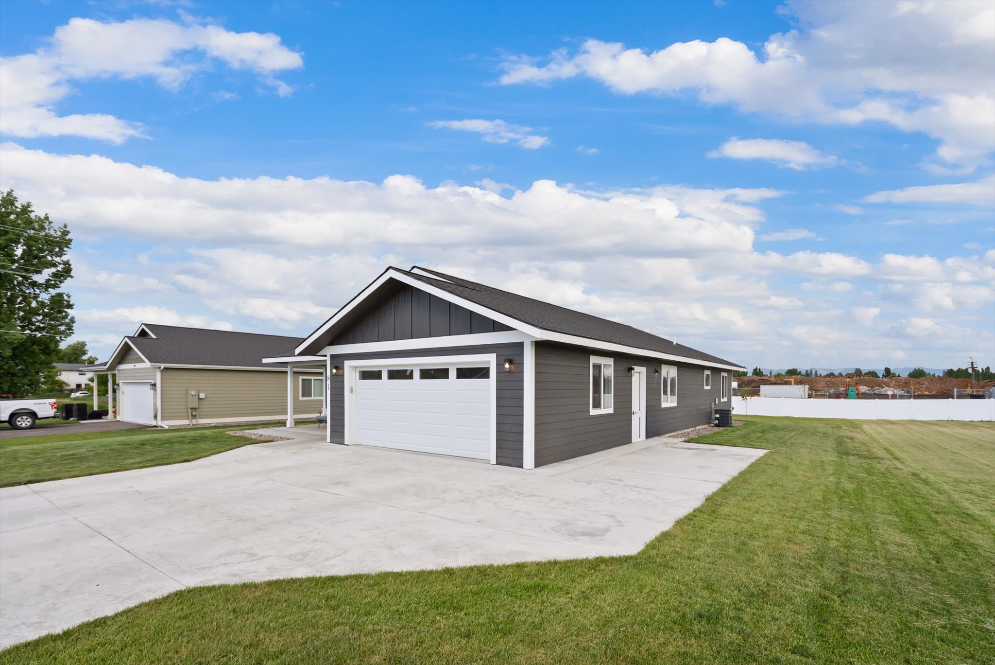 Gray single-story home with a white garage, broad concrete driveway, and green lawn.