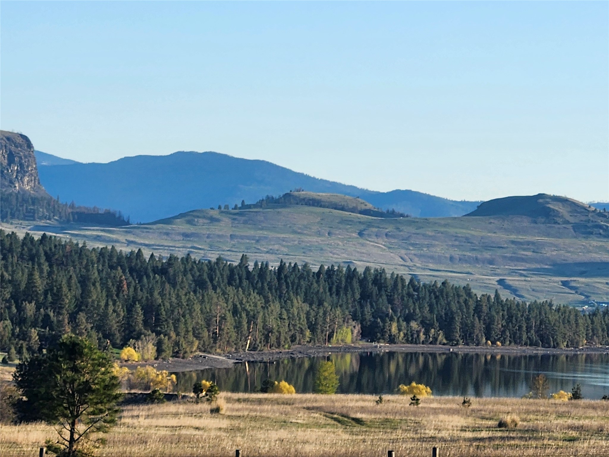 Lake reflecting a forest, with open fields and layered hills in the background.